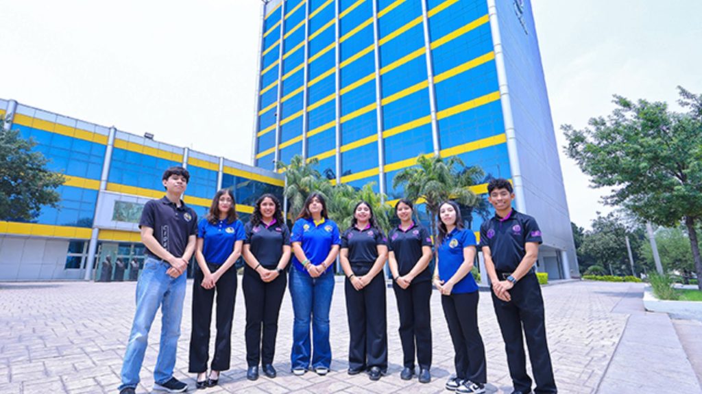 Group of Students Standing in a Line Outside a Blue and Yellow Modern Building, Posing for a Photo. - Los Industriales